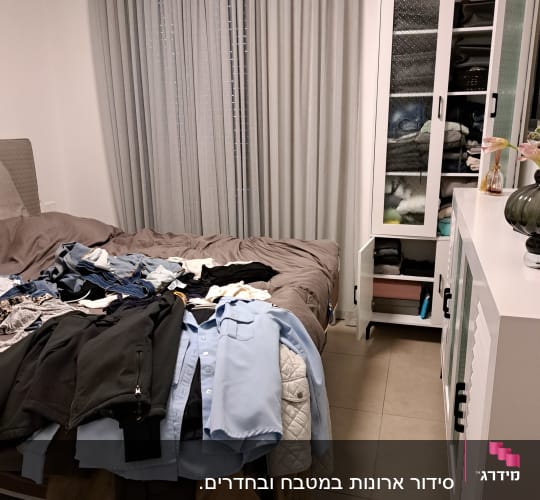 בגדים מסודרים על מיטה וארון פתוח עם בגדים מקופלים